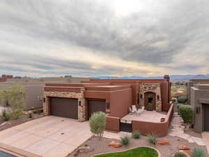 Adobe home featuring stone siding, concrete driveway, stucco siding, a garage, and a mountain view