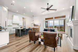 Living area featuring light wood finished floors, a ceiling fan, a chandelier, a glass covered fireplace, and recessed lighting