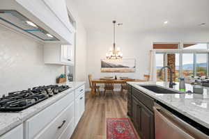 Kitchen featuring light stone counters, custom exhaust hood, white cabinetry, dishwasher, and decorative light fixtures