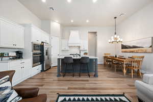 Kitchen featuring white cabinets, decorative light fixtures, appliances with stainless steel finishes, a kitchen breakfast bar, and open floor plan