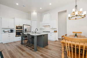 Kitchen with a breakfast bar area, white cabinetry, a chandelier, a kitchen island with sink, and stainless steel appliances