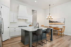 Kitchen with white cabinets, light stone counters, an island with sink, decorative backsplash, and pendant lighting