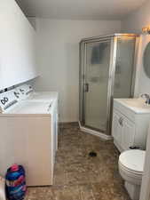 Bathroom featuring a stall shower, vanity, stone finish floors, and washing machine and clothes dryer