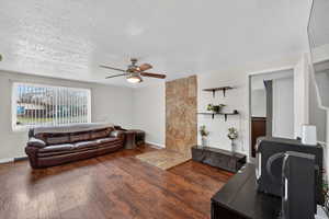 Living room featuring a textured ceiling, dark wood-style flooring, ceiling fan, and a desk