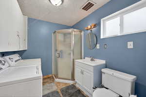 Full bathroom featuring a stall shower, vanity, a textured ceiling, and washer and dryer