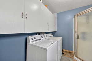 Laundry room featuring independent washer and dryer, a textured ceiling, and cabinet space