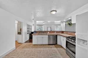 Kitchen with white cabinetry, a textured ceiling, stainless steel appliances, light countertops, and tasteful backsplash