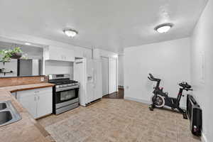 Kitchen featuring white cabinetry, stainless steel gas range oven, a textured ceiling, light countertops, and white fridge with ice dispenser