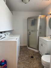 Bathroom featuring a shower stall, vanity, a textured ceiling, stone finish floors, and washer and clothes dryer
