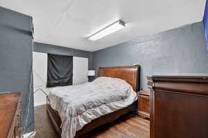 Bedroom with a textured wall, dark wood-style flooring, and a textured ceiling
