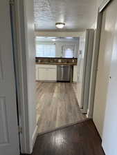 Kitchen featuring dark wood-style flooring, stainless steel dishwasher, freestanding refrigerator, a textured ceiling, and dark countertops