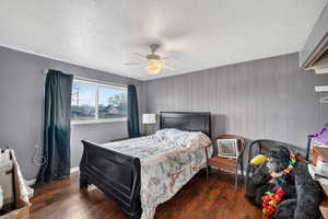 Bedroom featuring a textured ceiling, dark wood finished floors, a ceiling fan, and wood walls