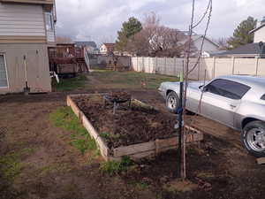 Fenced backyard featuring a garden, a fire pit, a wooden deck, and stairway