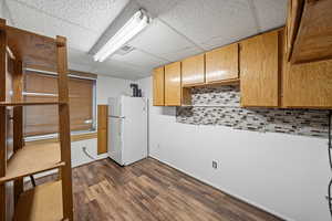 Kitchen with freestanding refrigerator, light countertops, dark wood-type flooring, a paneled ceiling, and decorative backsplash