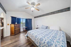 Bedroom with lofted ceiling, dark wood-type flooring, ceiling fan, and arched walkways