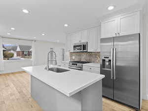 Kitchen with appliances with stainless steel finishes, a center island with sink, white cabinetry, light wood finished floors, and recessed lighting