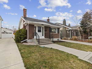 Bungalow featuring brick siding, a front yard, an outbuilding, and a detached garage