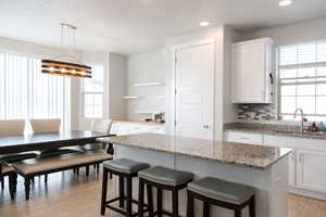 Kitchen with white cabinets, pendant lighting, a breakfast bar area, light stone counters, and recessed lighting