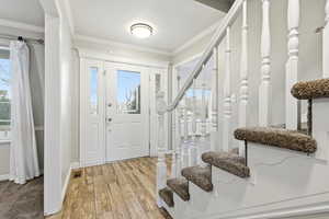 Foyer entrance featuring stairway, light wood-type flooring, ornamental molding, and healthy amount of natural light