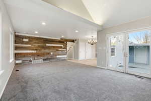 Unfurnished living room with wooden walls, an accent wall, a chandelier, stairs, and light carpet