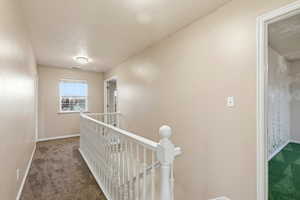 Hallway featuring an upstairs landing, dark colored carpet, and a textured ceiling