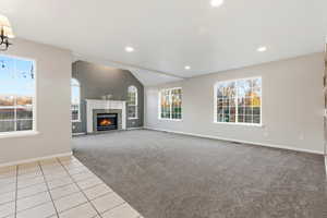 Unfurnished living room featuring light colored carpet, a brick fireplace, vaulted ceiling, recessed lighting, and light tile patterned floors