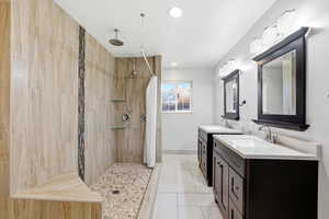 Bathroom featuring two vanities, a tile shower, recessed lighting, and light tile patterned floors