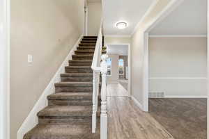 Stairs with wood finished floors, ornamental molding, and carpet floors