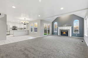 Unfurnished living room featuring a brick fireplace, light carpet, plenty of natural light, vaulted ceiling, and recessed lighting