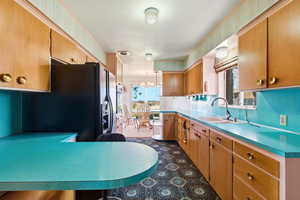 Kitchen featuring black fridge with ice dispenser, pendant lighting, a chandelier, light countertops, and a peninsula