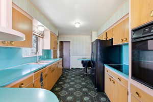 Kitchen with wallpapered walls, black appliances, light brown cabinetry, light countertops, and range hood