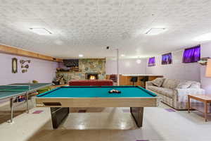 Rec room with concrete block wall, tile patterned floors, a stone fireplace, and billiards