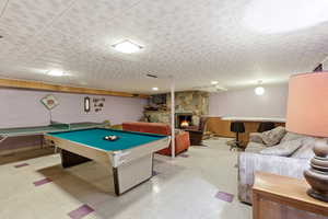 Rec room with light flooring, concrete block wall, a stone fireplace, billiards, and wainscoting
