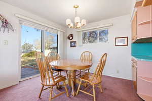 Carpeted dining area with a chandelier and baseboards