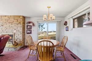 Carpeted dining space with plenty of natural light, a stone fireplace, and a chandelier