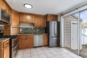 Kitchen with stainless steel appliances, brown cabinets, light stone countertops, tasteful backsplash, and a textured ceiling