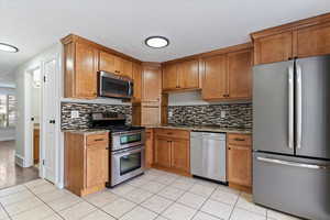 Kitchen featuring stainless steel appliances, light stone counters, brown cabinetry, light tile patterned floors, and a textured ceiling
