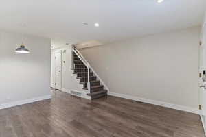Unfurnished living room featuring dark wood-style flooring and stairs