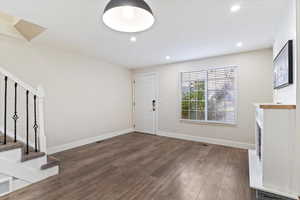 Entryway with stairs, dark wood-type flooring, recessed lighting, and a fireplace with raised hearth