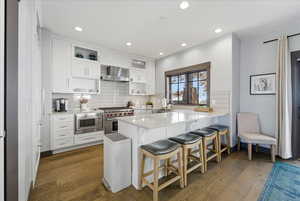 Kitchen with white cabinets, a kitchen bar, dark wood-style floors, a peninsula, and recessed lighting