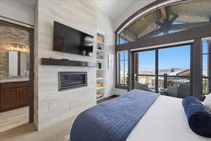 Bedroom with light carpet, access to exterior, a tile fireplace, connected bathroom, and high vaulted ceiling