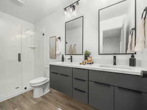 Full bathroom with double vanity, a shower stall, and light wood-type flooring