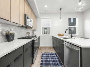 Kitchen with modern cabinets, appliances with stainless steel finishes, pendant lighting, light stone counters, and recessed lighting