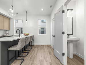 Kitchen featuring a breakfast bar, decorative light fixtures, light brown cabinetry, light wood-type flooring, and a peninsula