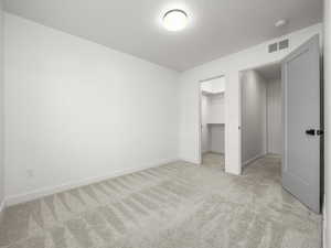 Unfurnished bedroom with light carpet and a walk in closet