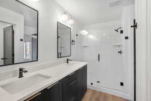 Bathroom with double vanity, a shower stall, and light wood-style floors