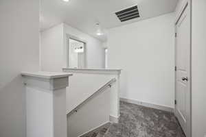 Hall featuring an upstairs landing and dark carpet