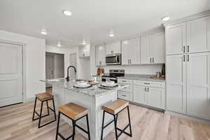 Kitchen featuring light stone counters, a kitchen breakfast bar, a center island with sink, appliances with stainless steel finishes, and light wood-style floors