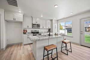 Kitchen with white cabinets, stainless steel appliances, a kitchen bar, light stone countertops, and light wood-style floors
