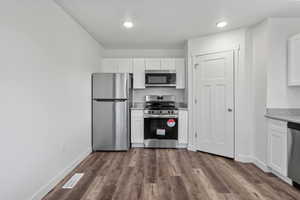 Kitchen with white cabinets, stainless steel appliances, dark wood-style floors, and light stone counters